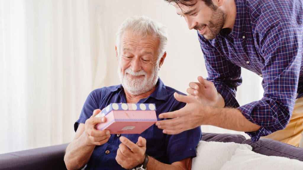 Father gets a present from his adult son sitting in living room. gift ideas for older men
