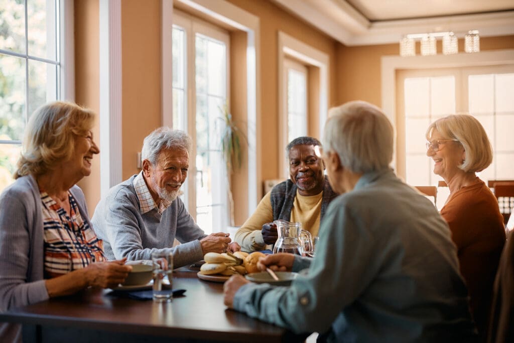 Group of senior people enjoying conversation and making new friends during lunch at dining table at senior living community