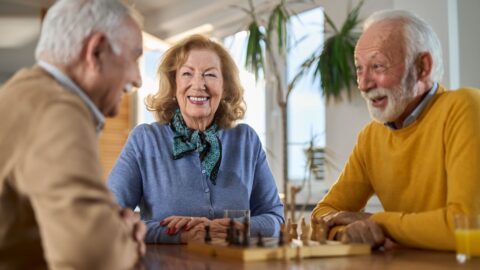 Happy senior friends playing chess at continuing care retirement community; Questions to Ask When Touring CCRCs