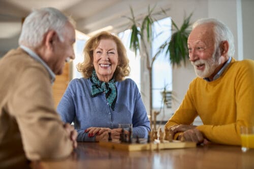 Happy senior friends playing chess at continuing care retirement community; Questions to Ask When Touring CCRCs