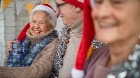 Happy senior friends sitting indoors in community center and celebrating Christmas. Happy senior friends sitting indoors in a senior living community and celebrating Christmas, avoiding being alone during the holiday season