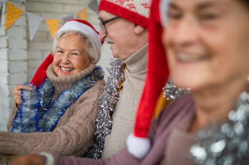 Happy senior friends sitting indoors in a senior living community and celebrating Christmas.