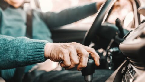 Close up of senior man holding one hand on gearshift and other on steering wheel while sitting in his car. Selective focus on hand. Why You Should Move to a CCRC Before You Stop Driving